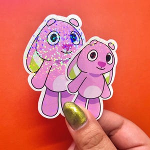 May include: Two pink glitter bunny stickers with green ears. The larger bunny has a white outline and the smaller bunny has a black outline.