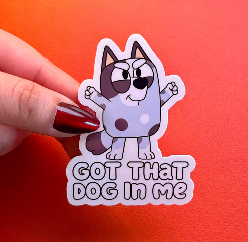 May include: A die-cut sticker featuring a light blue and dark grey cartoon dog with a determined expression, standing with arms raised. Below the character, the text reads "GOT THAT DOG IN ME" in bold, black, rounded capital letters.