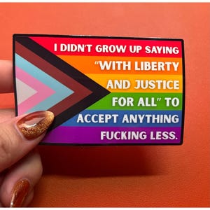 Könnte beinhalten: Ein rechteckiger Aufkleber mit dem Design der Progress Pride Flagge und einem schwarzen Rand. Der Text lautet: I DIDN'T GROW UP SAYING "WITH LIBERTY AND JUSTICE FOR ALL" TO ACCEPT ANYTHING FUCKING LESS. Die Farben umfassen Rot, Orange, Gelb, Grün, Blau, Lila, Weiß, Rosa, Hellblau, Braun und Schwarz.