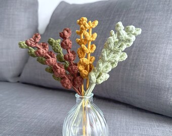 May include: A small glass vase with a textured surface holds a bouquet of crocheted flowers in shades of green, brown, and yellow.