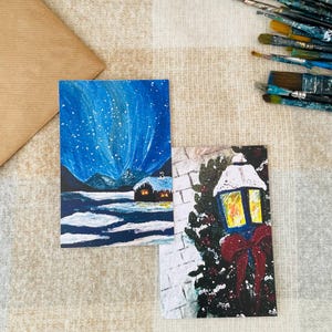 Ensemble de 2 tirages d'art de cartes postales de vacances d'hiver peintes à la main, chalet de Noël confortable, paysage enneigé et lanterne de Noël