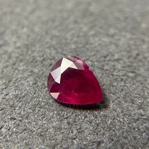 Puede incluir: Una piedra preciosa de color rojo intenso en forma de pera con un corte facetado.