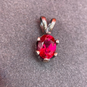 May include: A silver pendant with a red gemstone set in a prong setting.
