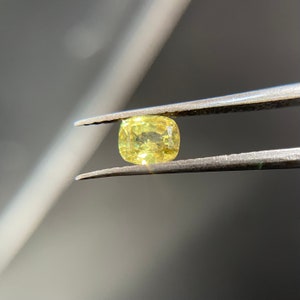 Könnte beinhalten: Ein gelber Edelstein mit Kissen-Schliff, gehalten von einer Pinzette.