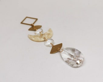 May include: A gold geometric pendant with a clear crystal teardrop, a white crescent moon, and a gold square.