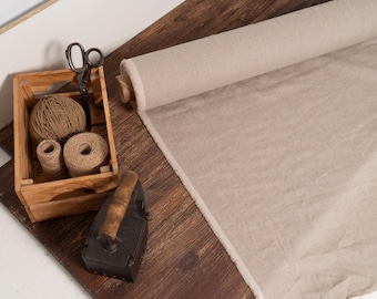 May include: A rustic scene featuring a roll of beige fabric, a wooden crate with twine and scissors, and a vintage iron. The fabric is unrolled on a wooden surface, suggesting a craft or sewing project.