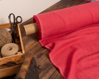 May include: A roll of vibrant red fabric with a textured appearance, alongside a wooden crate containing twine, scissors, and spools. An antique iron rests nearby, suggesting a crafting or sewing theme.