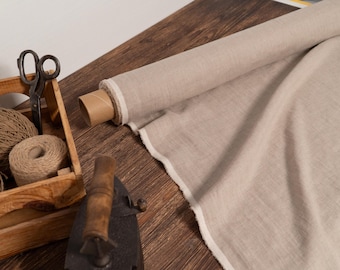 May include: A roll of beige fabric with a raw edge, alongside a wooden box containing twine and scissors. An antique iron rests on a wooden surface, suggesting a sewing or crafting theme.