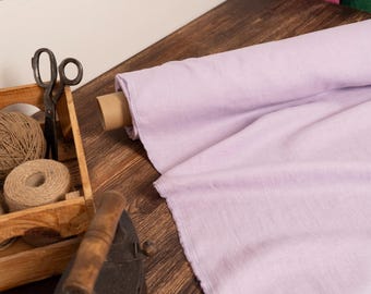May include: A roll of light purple fabric sits on a wooden surface next to a wooden crate filled with twine and scissors. An antique iron rests nearby, suggesting a crafting or sewing theme.