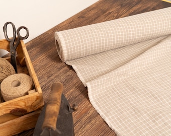 May include: A roll of beige and white checkered fabric sits next to a wooden crate filled with twine and scissors. An antique iron rests nearby. The scene suggests a crafting or sewing theme.