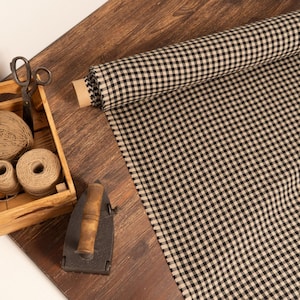 May include: A roll of black and white checkered fabric lies next to a wooden crate filled with twine and scissors. An antique iron rests nearby on a dark wooden surface. The scene evokes a rustic, vintage aesthetic, suitable for crafting or home decor.