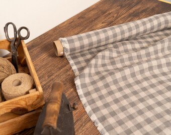 May include: A roll of gray and white checkered fabric sits on a wooden surface next to a wooden box filled with twine, scissors, and an iron. The fabric is unrolled, showing the pattern.
