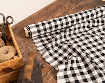 May include: A roll of black and white gingham fabric is partially unrolled on a wooden surface. A wooden crate contains twine and scissors. An antique iron is in the foreground. The scene suggests a craft or sewing project.