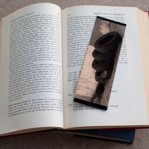 Puede incluir: Un primer plano de un libro con un marcapáginas. El marcapáginas es una fotografía de una pila de neumáticos contra una pared de madera. El libro está abierto en una página con texto sobre literatura inglesa.
