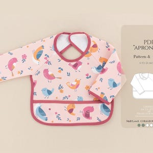 Peut inclure: Un bavoir rose pour bébé à manches longues, orné d'illustrations d'oiseaux colorés. Le bavoir a une poche en bas et une bordure rose foncé contrastante. L'image comprend également un patron et un tutoriel pour le bavoir, pour les bébés de 6 à 24 mois.
