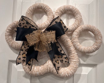 May include: A white and brown yarn wreath shaped like a paw print with a black and brown leopard print bow.
