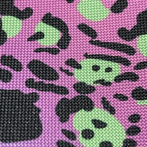 May include: Purple fabric with a black and green abstract pattern. The pattern resembles a series of overlapping circles and swirls.