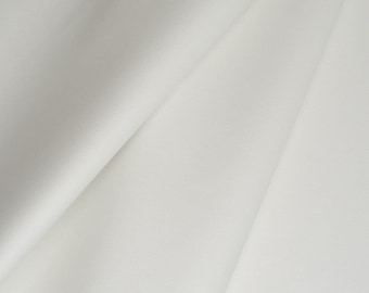 May include: A close-up of a smooth, white fabric with a subtle texture. The fabric is folded in a way that creates soft, flowing lines.