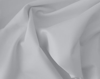 May include: A close-up of a smooth, white fabric with soft folds and wrinkles. The fabric has a subtle texture and a slightly gray tone.