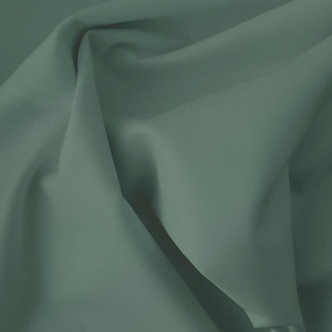 Pode incluir: Close-up de um tecido verde sálvia dobrado. O material tem uma textura sutil e drapeja em dobras suaves, criando sombras e destaques. A cor é um tom suave e terroso, adequado para vários projetos têxteis.