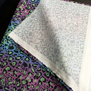 May include: A close-up of a fabric with a leopard print pattern in shades of blue, purple, green, and black. The fabric is folded over, revealing a white lining.