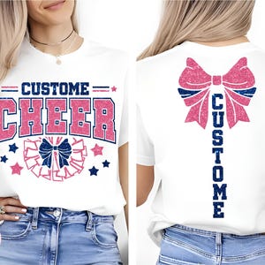 May include: White t-shirt with "CUSTOM CHEER" in pink and blue glitter text. The front design includes a cheer bow and stars. The back of the shirt features a large pink bow and the word "CUSTOM" in blue glitter.