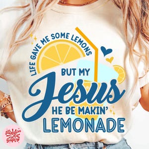 Può includere: T-shirt color crema con un design grafico raffigurante una fetta di limone, un bicchiere di limonata e la scritta "Life gave me some lemons but my Jesus he be makin' lemonade."