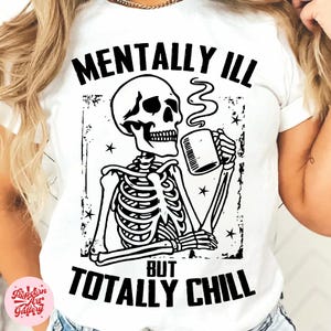 Puede incluir: Camiseta blanca con un diseño de esqueleto negro bebiendo de una taza. El texto dice "MENTALLY ILL BUT TOTALLY CHILL". El diseño incluye estrellas y un borde desgastado.