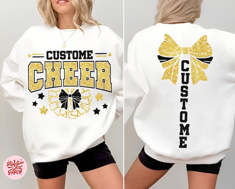 May include: White sweatshirt with "CUSTOM CHEER" in gold glitter lettering. The front features a bow and stars, while the back displays a large bow and the word "CUSTOM". A cheerleading-themed design.