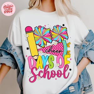 May include: White t-shirt with a colorful graphic design featuring a large yellow pencil, two pom-poms, and the words "cheer DAYS OF School" in a playful font. The design includes pink, blue, green, and yellow colors.