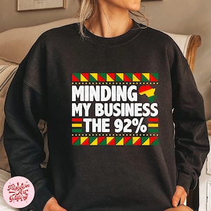 May include: Black sweatshirt with a colorful graphic design that says "Minding My Business The 92%".