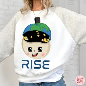 May include: White sweatshirt with grey sleeves. The design features a cartoon character wearing a globe-shaped hat with stars. The character has a smiling face and the word "RISE" in blue. A fun, whimsical design.