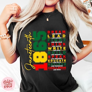 以下が含まれることがあります： 1865年と「Juneteenth」という単語が縦に積み重ねられたグラフィックデザインが施された黒いTシャツ。グラフィックには、「Dream」、「Lead」、「Fight」、「Think」、「Write」、「Build」、「Speak」、「Educate」、「Believe」、「Challenge」などのアクション動詞のリストも含まれており、各動詞は著名なアフリカ系アメリカ人の名前とペアになっています。