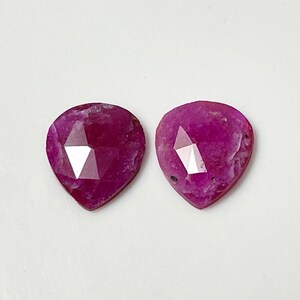 May include: Two pink ruby gemstones with a faceted heart shape.
