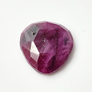May include: A deep pink ruby gemstone with a faceted heart shape.