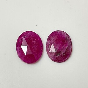 May include: Two pink oval-shaped gemstones with a faceted cut. The gemstones have a slightly cloudy appearance.