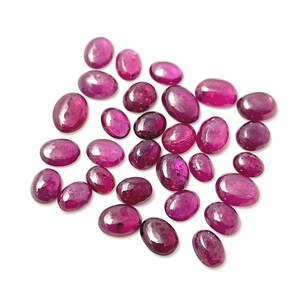 May include: A collection of oval-shaped, deep pink gemstones. The gemstones are scattered on a white background.