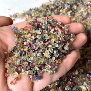 May include: A close-up of a hand holding a pile of small, colorful gemstones. The gemstones are a mix of red, yellow, green, and blue.