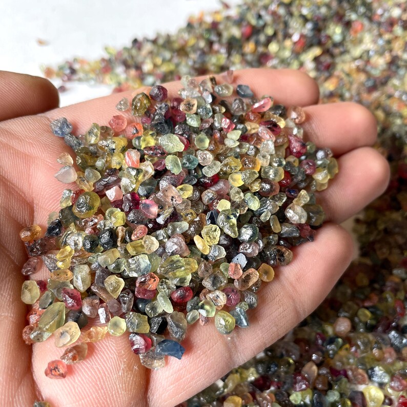 May include: A close-up of a hand holding a pile of small, colorful gemstones. The gemstones are a mix of red, yellow, green, and blue.
