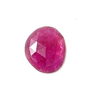 May include: A faceted ruby gemstone with a deep pink hue. The gemstone is cut in a unique, irregular shape and has a polished finish.