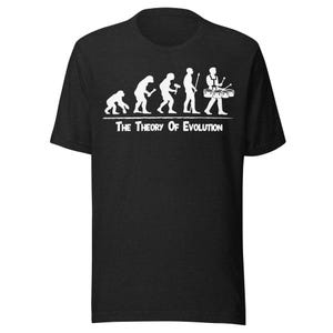 Könnte beinhalten: Ein schwarzes Kurzarm-T-Shirt mit einer weißen Grafik, die die menschliche Evolution darstellt und mit einer Person endet, die Schlagzeug spielt. Unter der Grafik steht der Text "The Theory Of Evolution" in weißer Schrift.