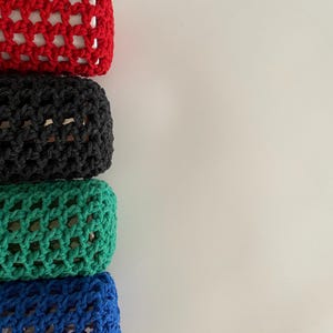 May include: Four crocheted cases in red, black, green, and blue. The cases are stacked on top of each other.