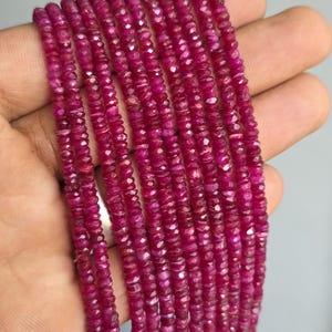 May include: A collection of multiple strands of small, faceted, deep magenta-colored ruby beads. Each bead features a circular shape with a reflective, multi-faceted surface, arranged in long, vertical rows that display a consistent, vibrant hue.