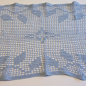 May include: A light blue crocheted blanket with a repeating floral pattern. The blanket is rectangular and has a delicate, open weave design. The edges are neatly finished, showcasing the craftsmanship.
