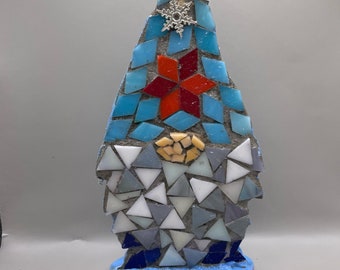 Op de afbeelding: Een blauwe mozaïekgnome met een rode ster en een zilveren sneeuwvlok op zijn muts. De gnome staat op een blauwe basis.