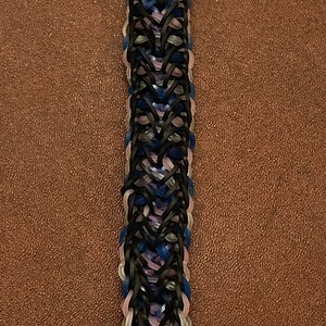 Puede incluir: Un brazalete de gomas elásticas de colores con un patrón negro, azul, rosa y gris.