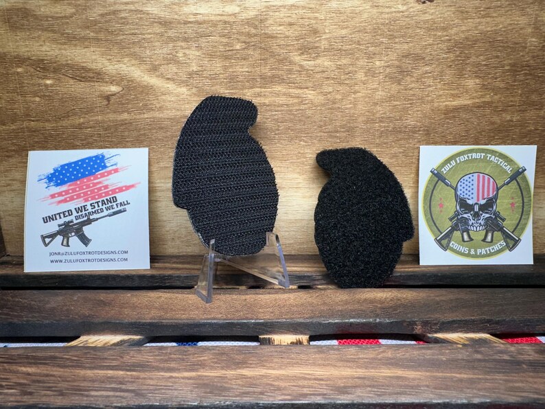 May include: Two black hook and loop patches, one shaped like a grenade and the other shaped like a skull with crossed rifles. The grenade patch has a white background and the skull patch has a green background with the text "Zulu Foxtrot Tactical Coins & Patches".