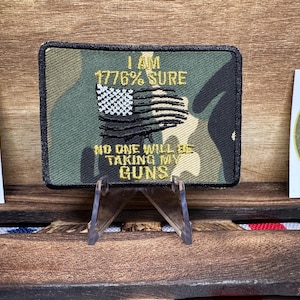 May include: A camouflage-patterned patch with the text "I am 1776% sure no one will be taking my guns" and a stylized American flag.