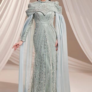 May include: A light green, floor-length gown with intricate beadwork and a high neckline. The dress features long, flowing sleeves and a cape-like overlay in a matching light blue hue. The gown is embellished with sparkling sequins.