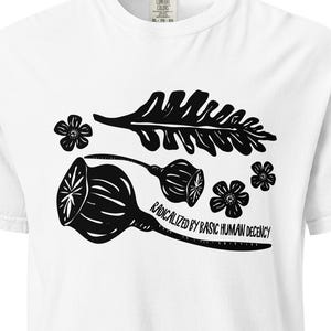 May include: White t-shirt with a black graphic design featuring botanical elements and the text "RADICALIZED BY BASIC HUMAN DECENCY". The design includes stylized leaves, flowers, and seed pods.